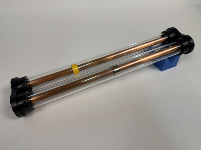 See-through demonstrator with a ring magnet and a yellow control ring surrounding copper tubes inside clear outer tubes.